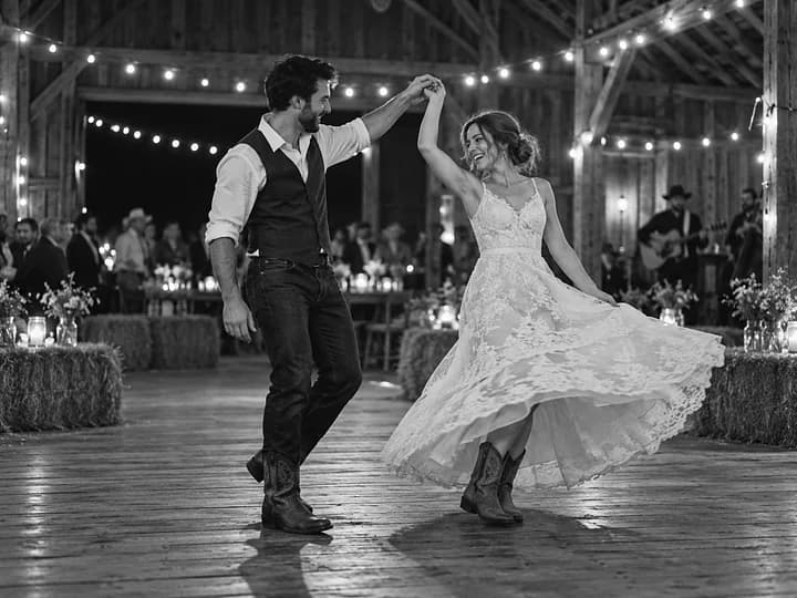 Black-and-white photo of a couple two-stepping in a barn strung with lights, her lace skirt flaring mid-twirl (AI photo, fictional people)