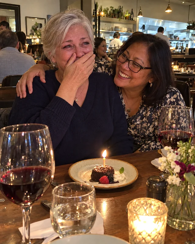 A woman around fifty laughs behind her hand at a restaurant table while her wife wraps an arm around her shoulders (AI photo, fictional people)