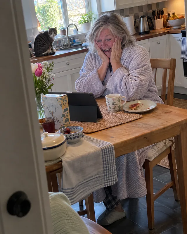 A woman in a bathrobe at her kitchen table, hands on her cheeks, looking at a tablet propped against a cereal box (AI photo, fictional person)