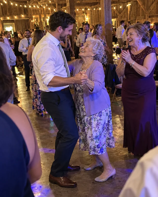 On a crowded barn dance floor, a groom dances with his grinning grandmother in a lilac cardigan while his mother in a plum dress laughs and claps beside them (AI photo, fictional people)